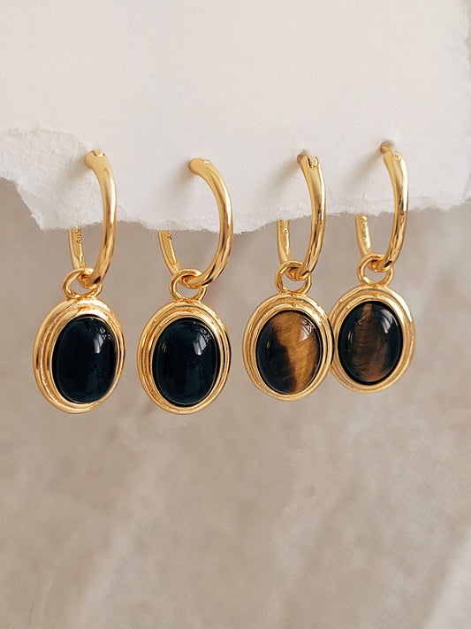 Close-up of gold vermeil dangle earrings with an oval black onyx gemstone or tiger's eye gemstone, minimalist and elegant style.
