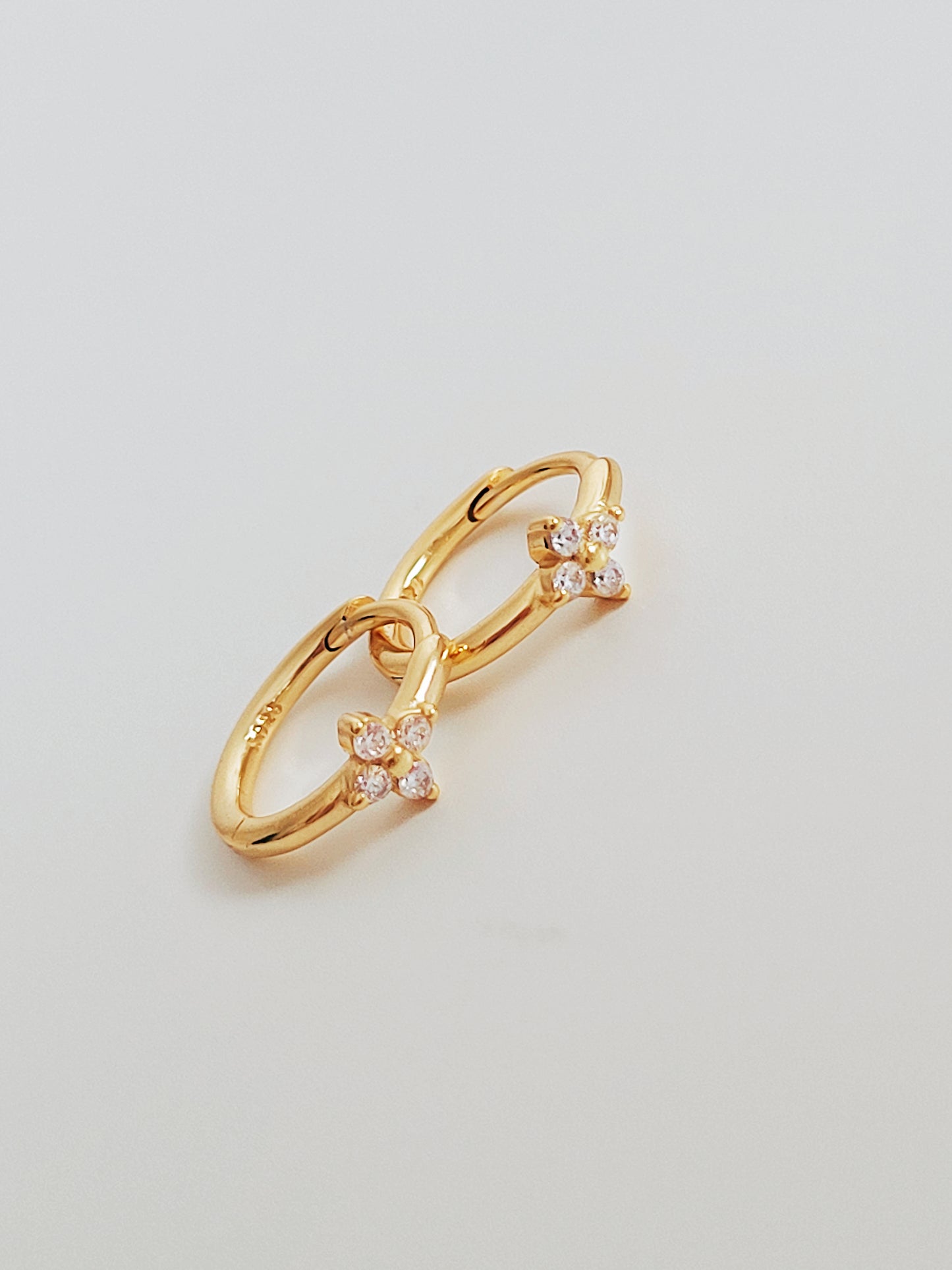 A pair of elegant Gold Clover Huggie Earrings with each earring composed of a small, clover-shaped charm attached to a huggie hoop.