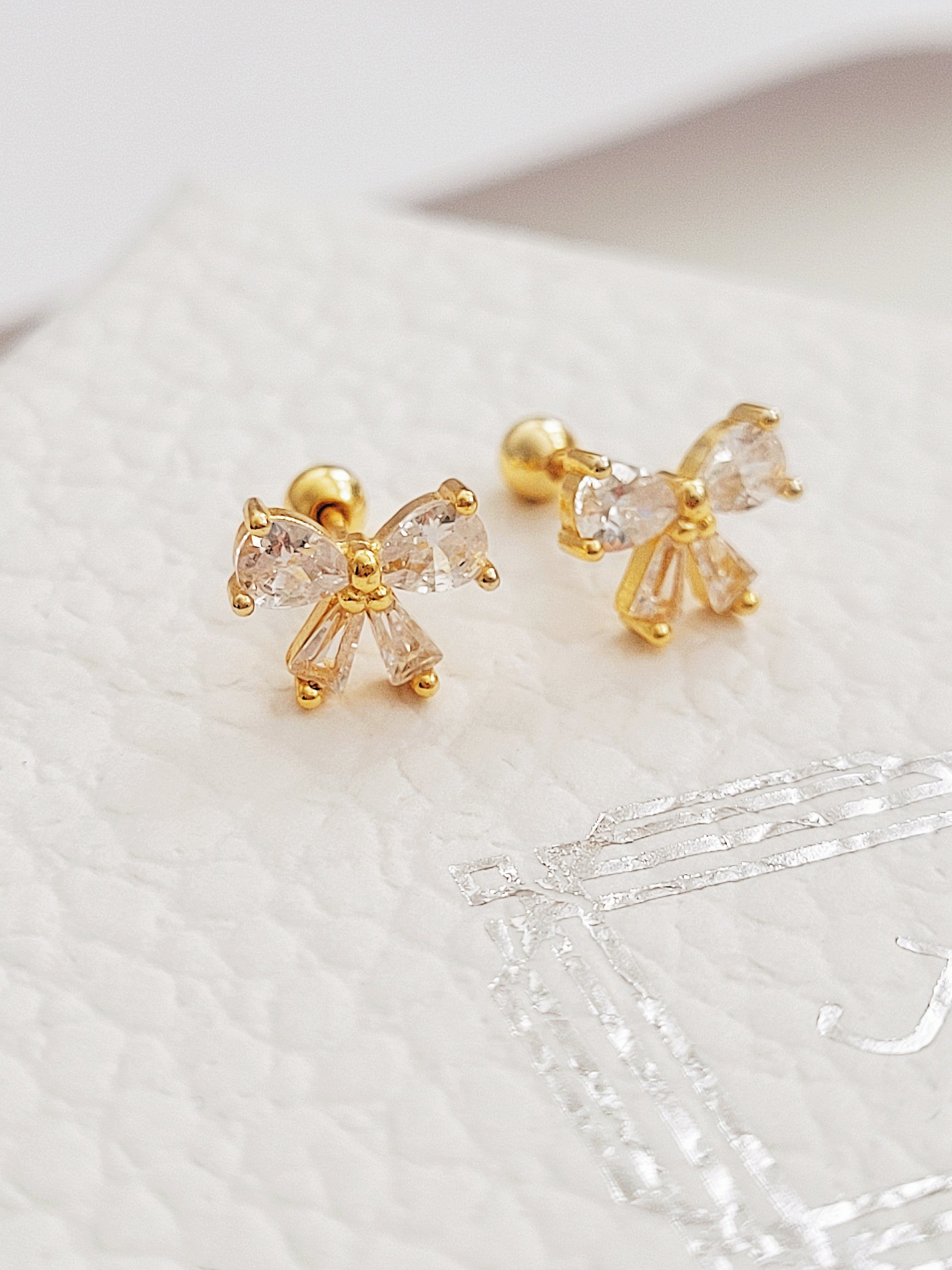 Close up of a woman's ear wearing dainty bow stud earrings with sparkling cubic zirconia and gold plating.