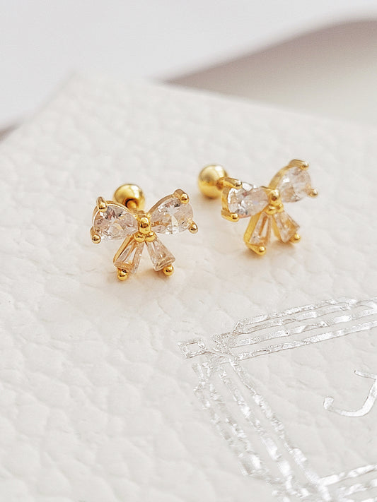 Close up of a woman's ear wearing dainty bow stud earrings with sparkling cubic zirconia and gold plating.