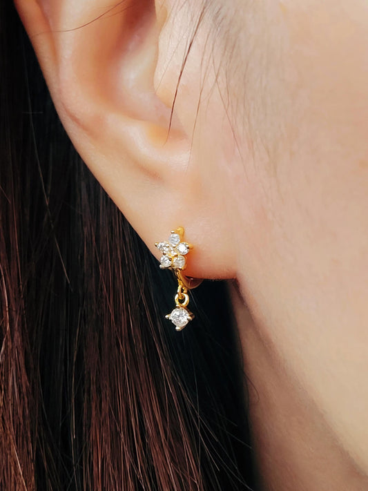Close-up of a woman wearing a gold flower huggie earrings with clear cubic zirconia stone dangle.