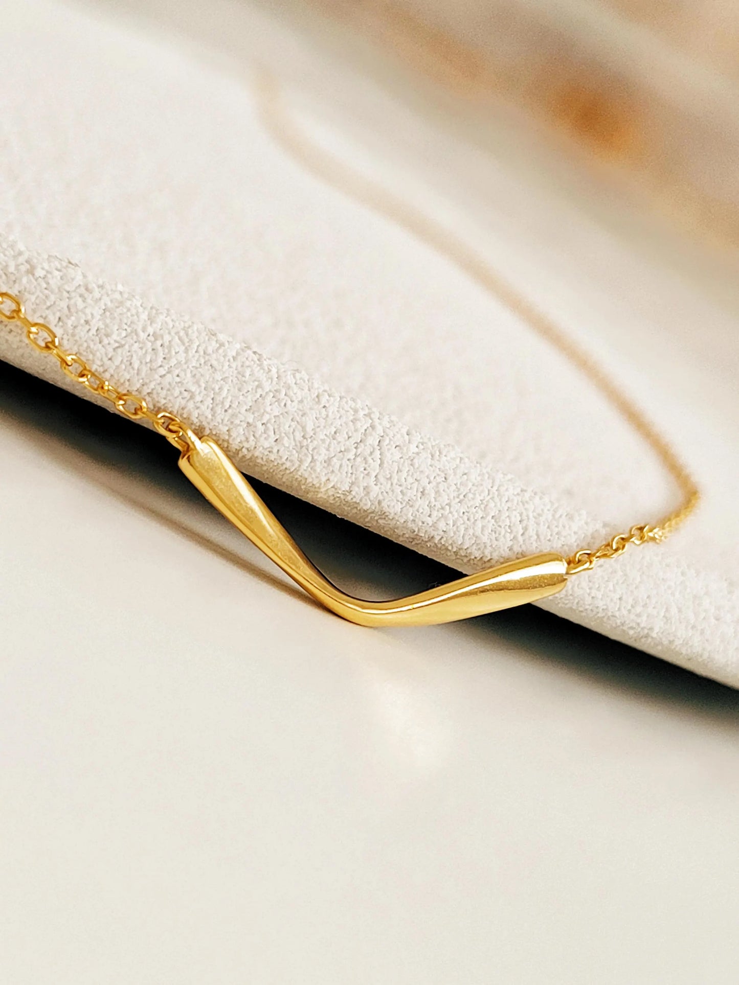 A gold necklace featuring a simple, curved pendant. The pendant is a single, smooth, curved line.