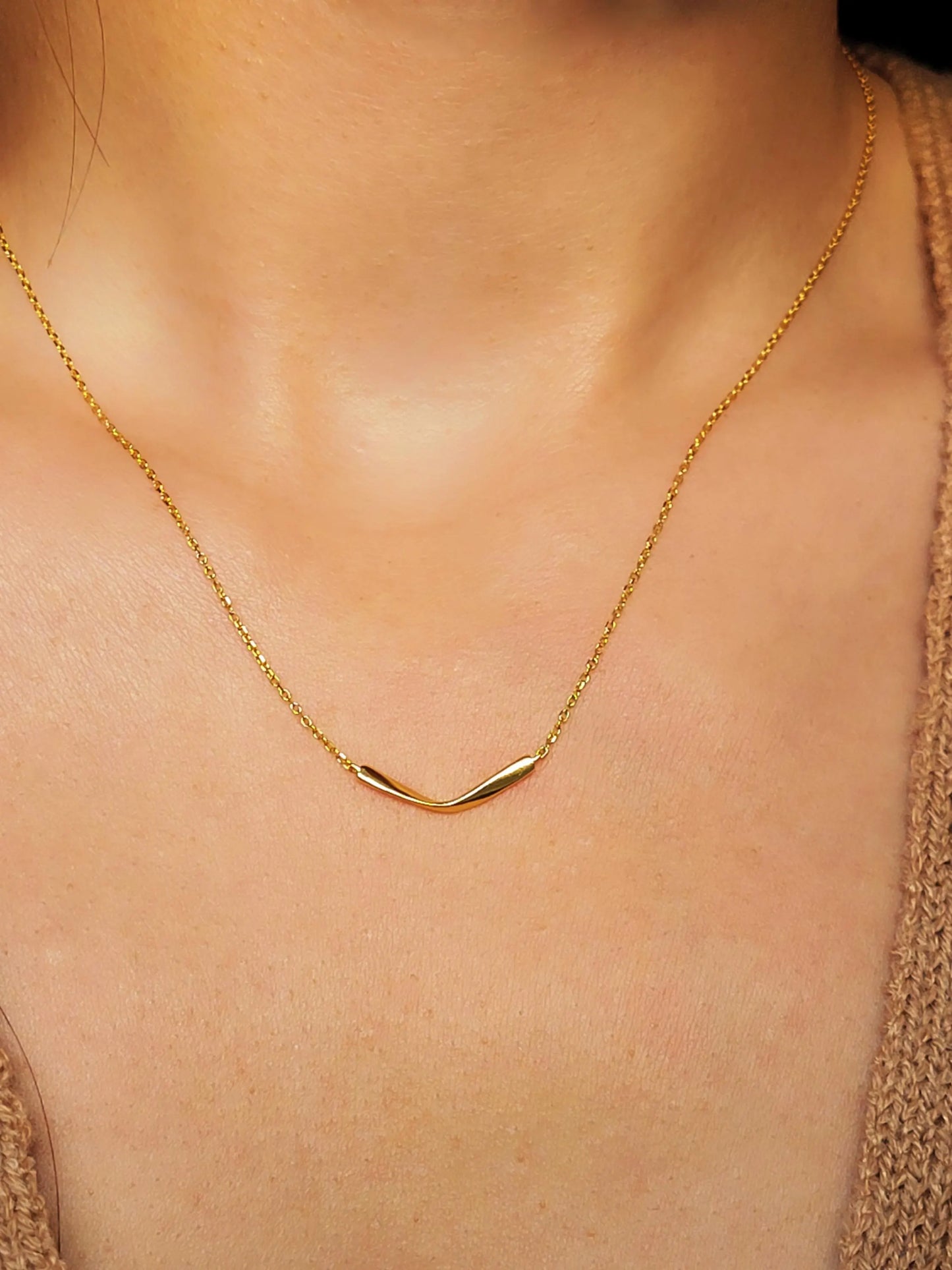 A delicate gold chain necklace with a simple, curved pendant worn on model.