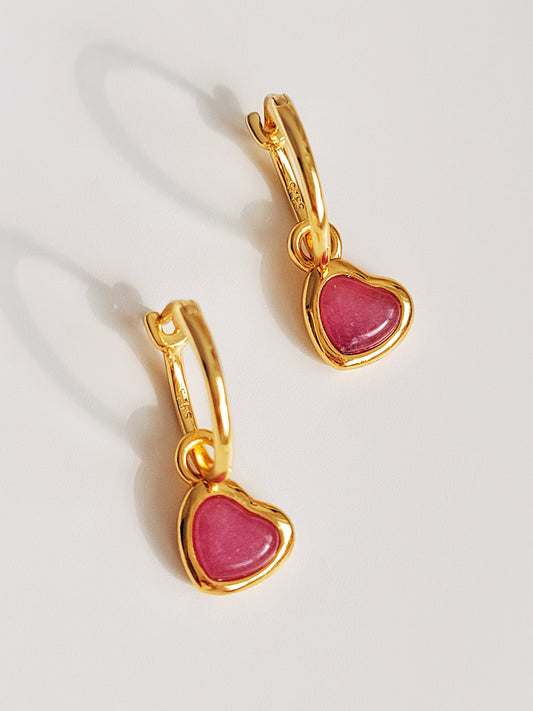 Gold heart earrings with pink gemstones on a light background