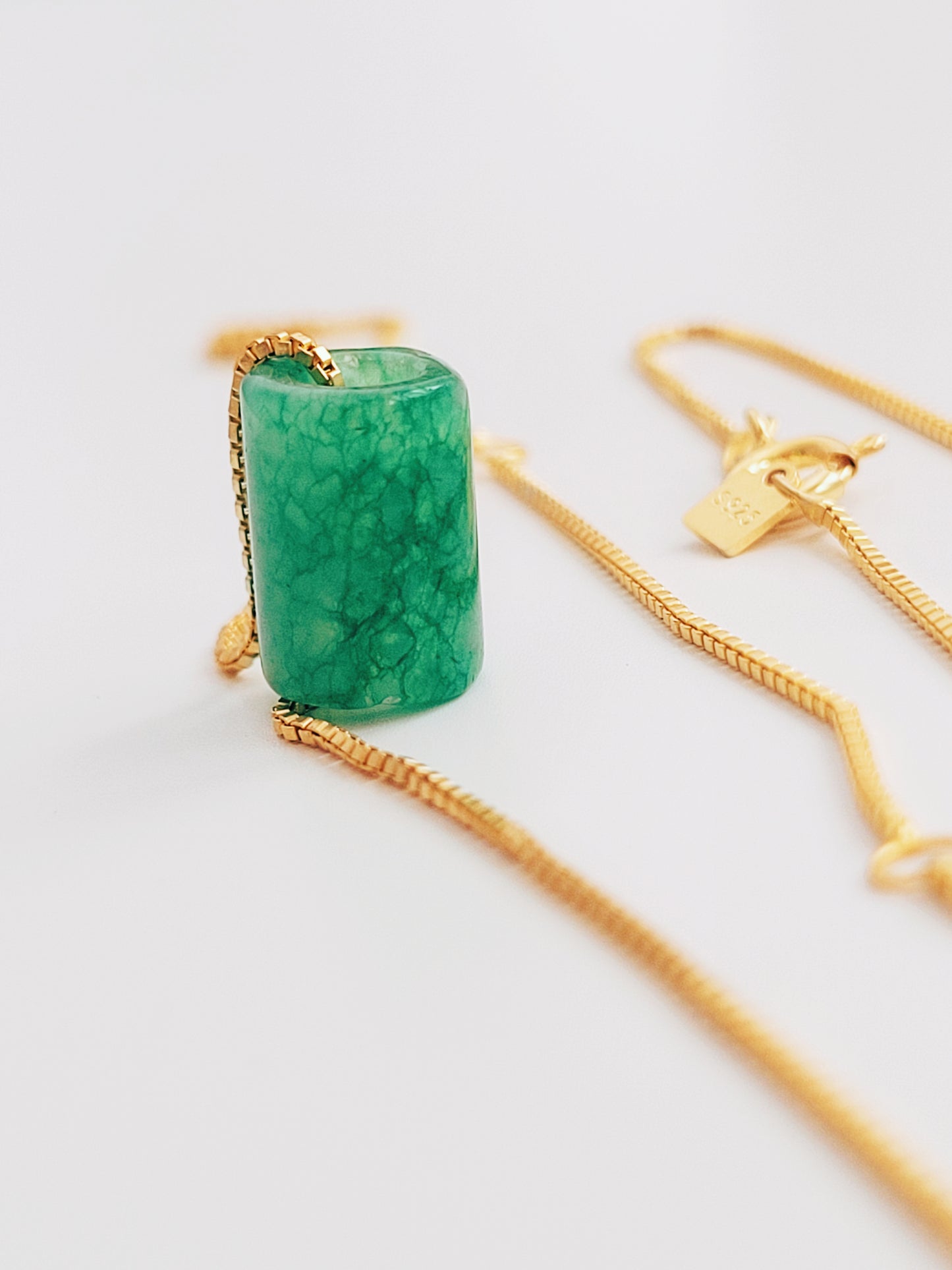 A natural green jade bead necklace with a polished finish, strung on a gold-plated sterling silver chain, offering a minimalist and elegant style.