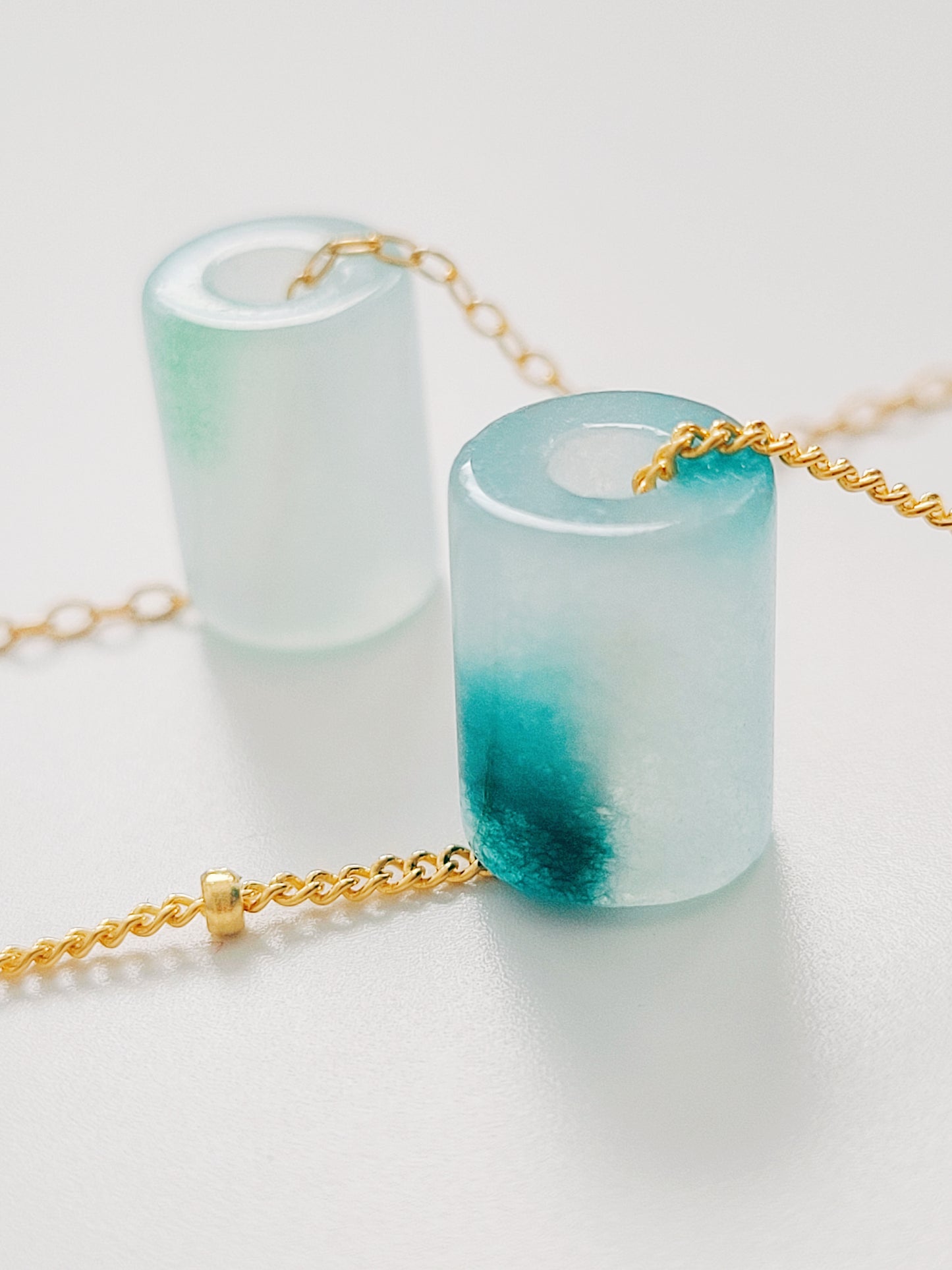A close-up of a pair of natural jade charm necklace, featuring an icy green jade or icy blue jade pendant on a gold-plated sterling silver chain, showcasing a delicate and elegant look.