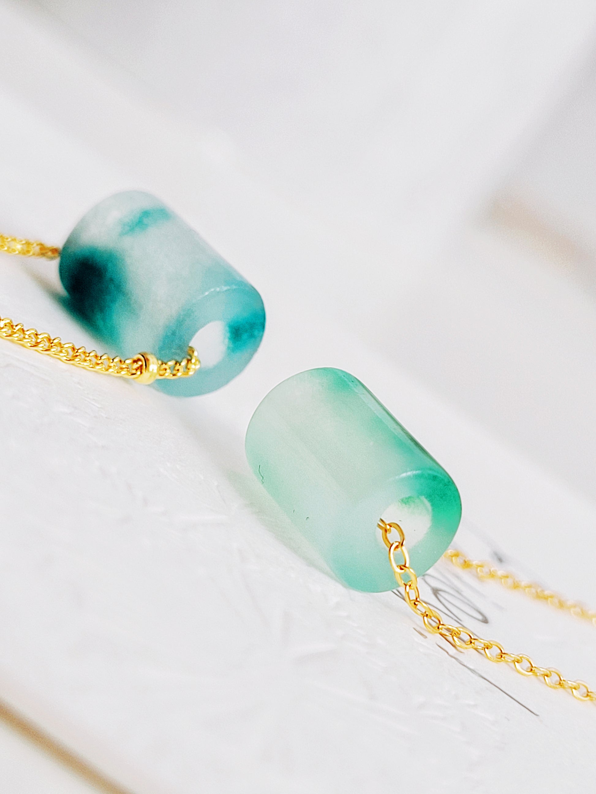 A close-up of a pair of natural jade charm necklace, featuring an icy green jade or icy blue jade pendant on a gold-plated sterling silver chain, showcasing a delicate and elegant look.