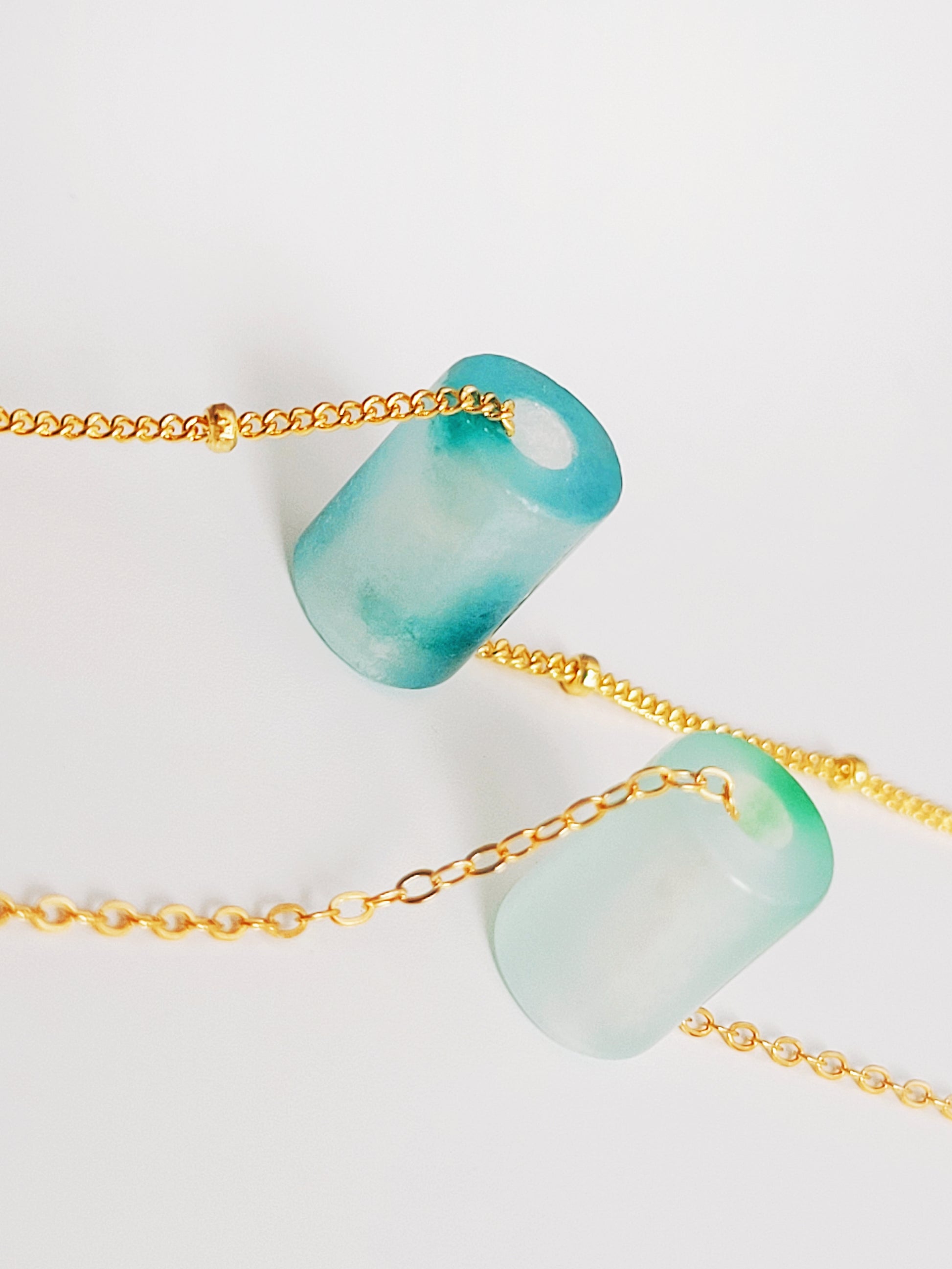 A close-up of a pair of natural jade charm necklace, featuring an icy green jade or icy blue jade pendant on a gold-plated sterling silver chain, showcasing a delicate and elegant look.