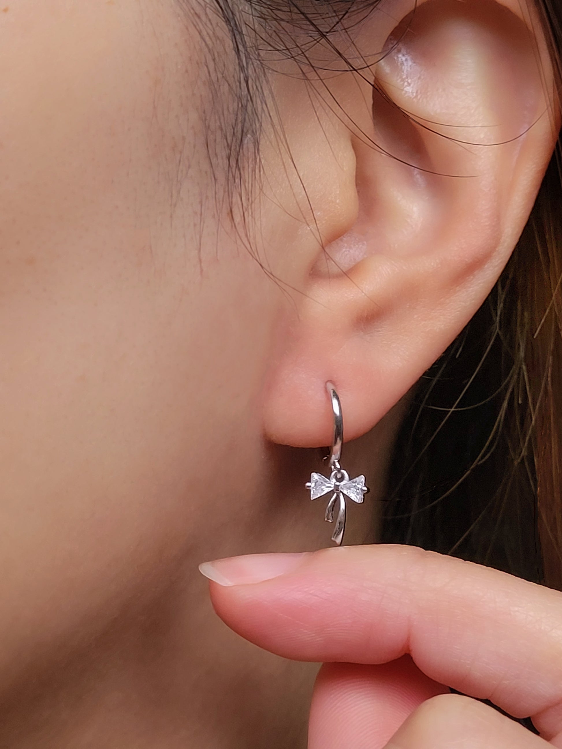 Close-up view of a woman's ear wearing silver ribbon bow earring with a dangling design, perfect for gifting to girlfriends, daughters, or loved ones.
