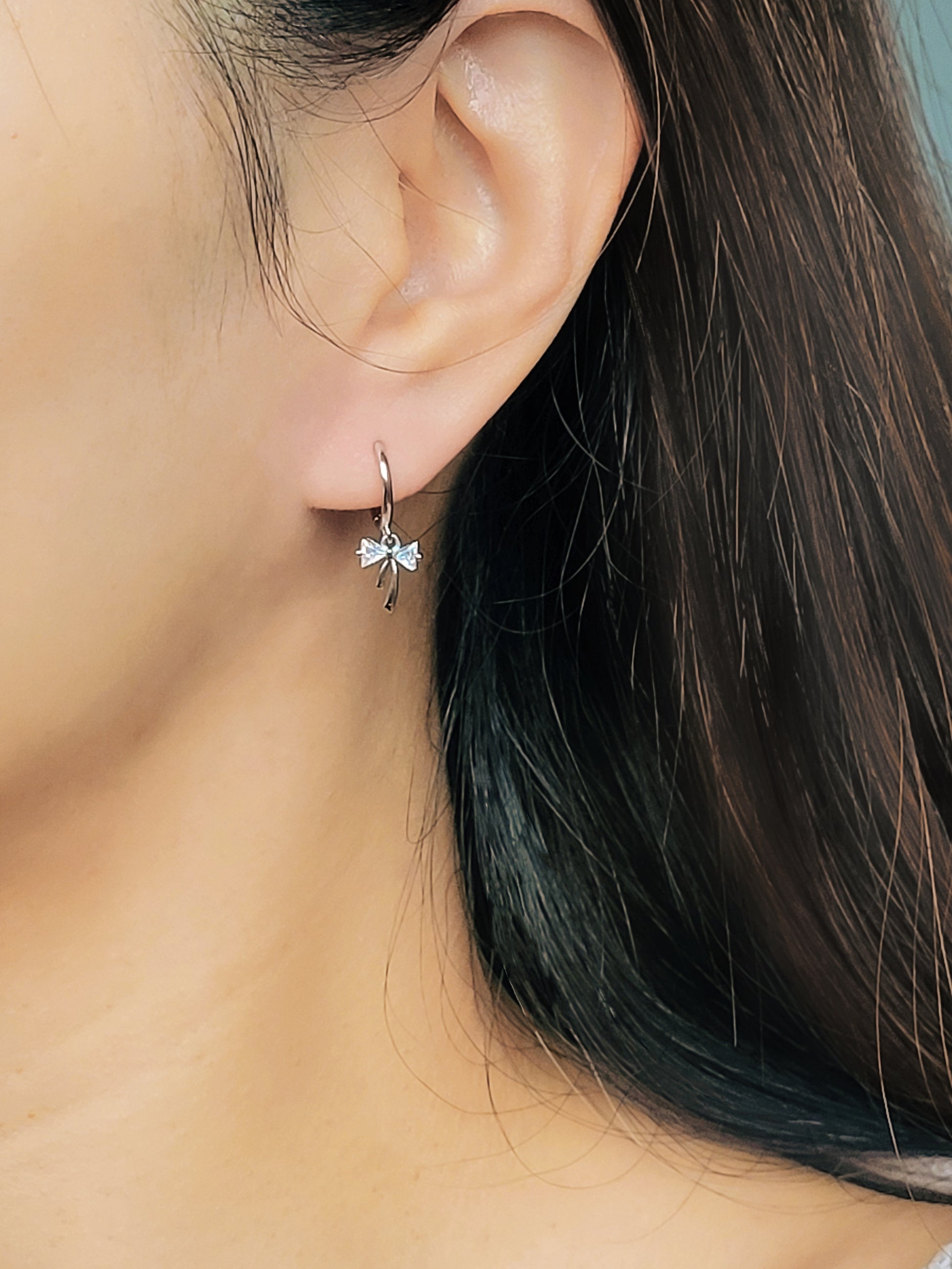 Close-up view of a woman's ear wearing silver ribbon bow earring with a dangling design, perfect for gifting to girlfriends, daughters, or loved ones.