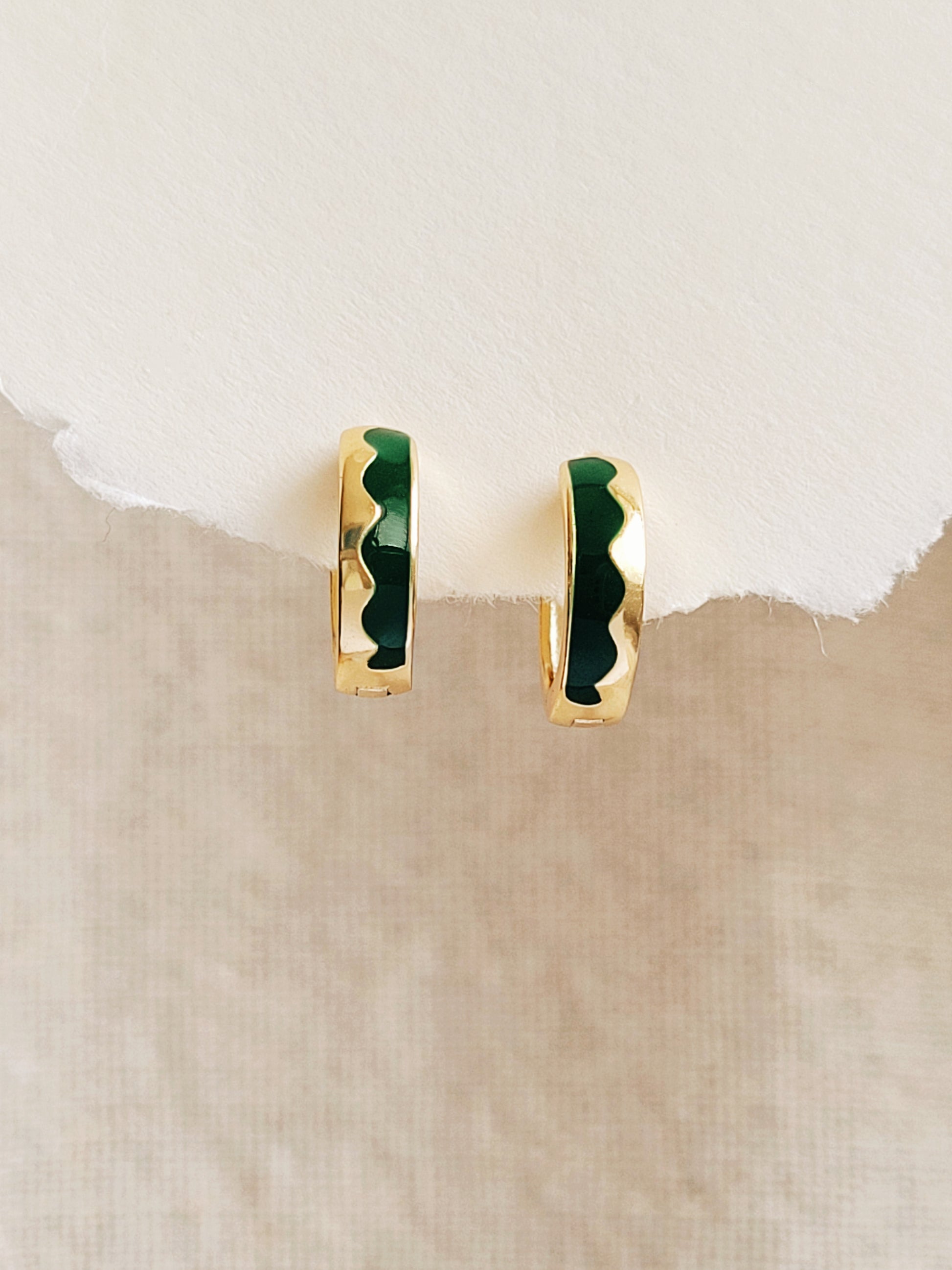 Gold hoop earrings with green enamel wavy pattern on a beige background