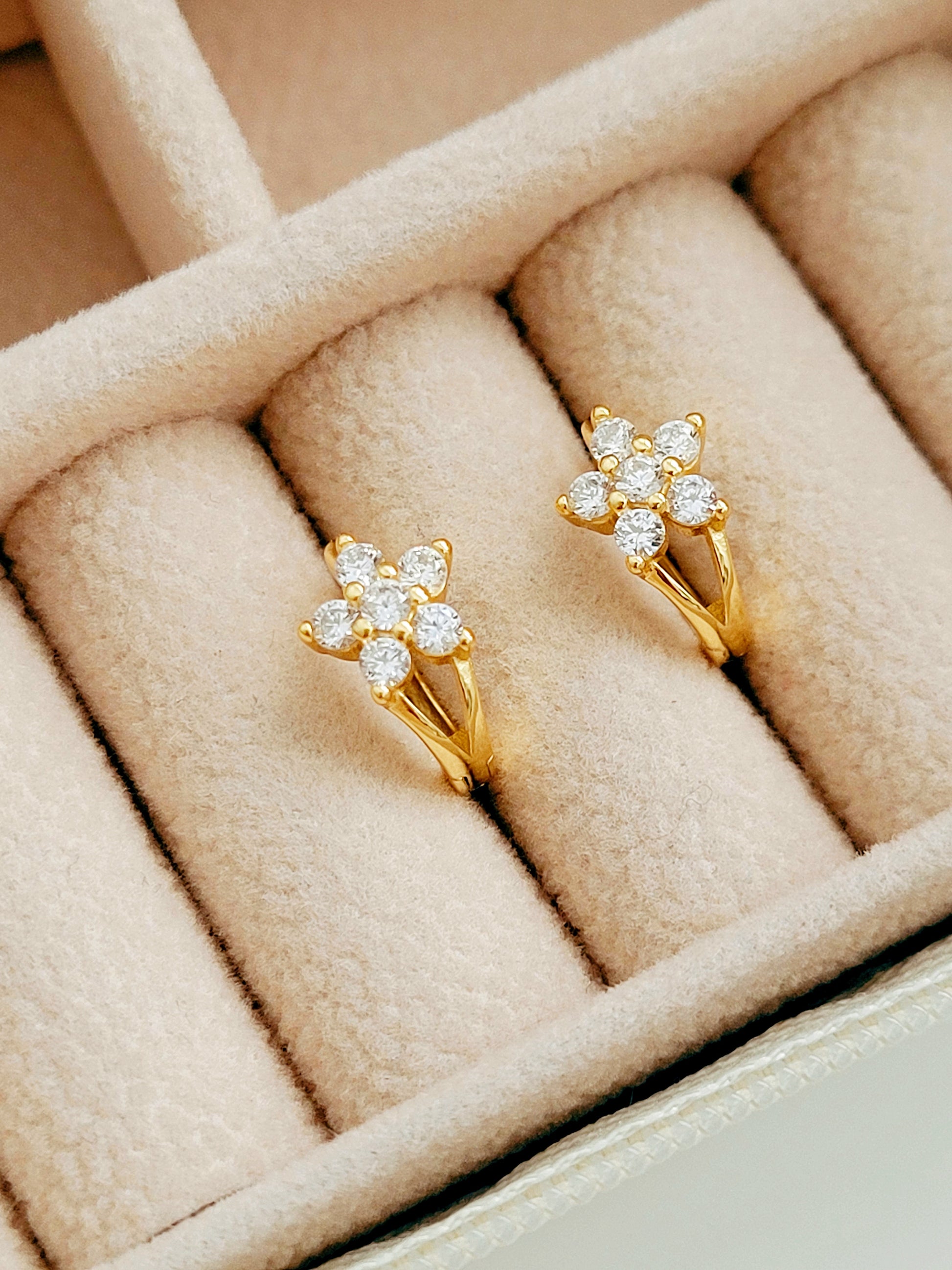 A pair of gold plated huggie hoop earrings with a floral design and cubic zirconia accents, displayed in a soft pink-lined box.