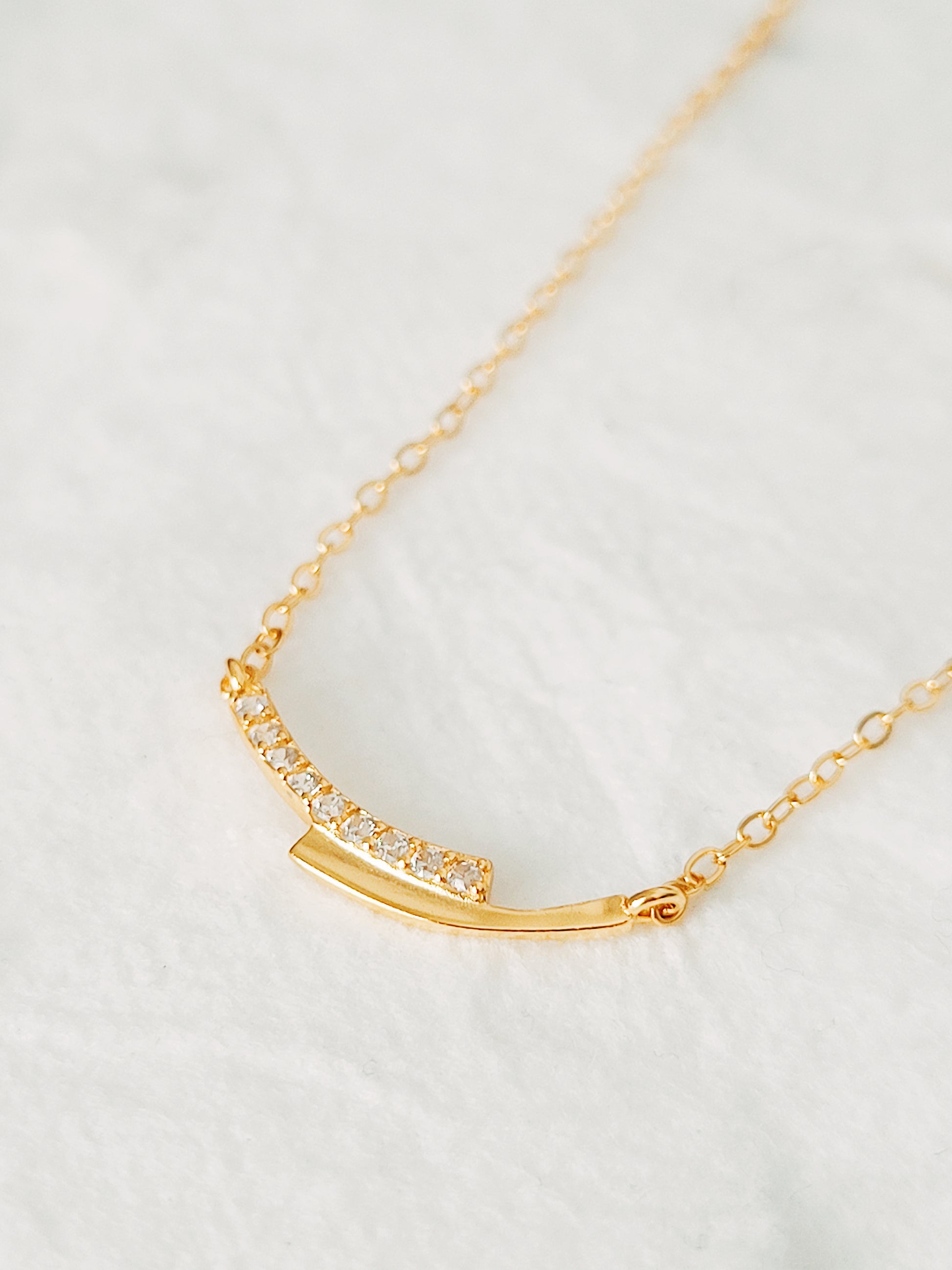 Close up of a simple gold bar necklace with cubic zirconia accents, symbolizes love and unity.