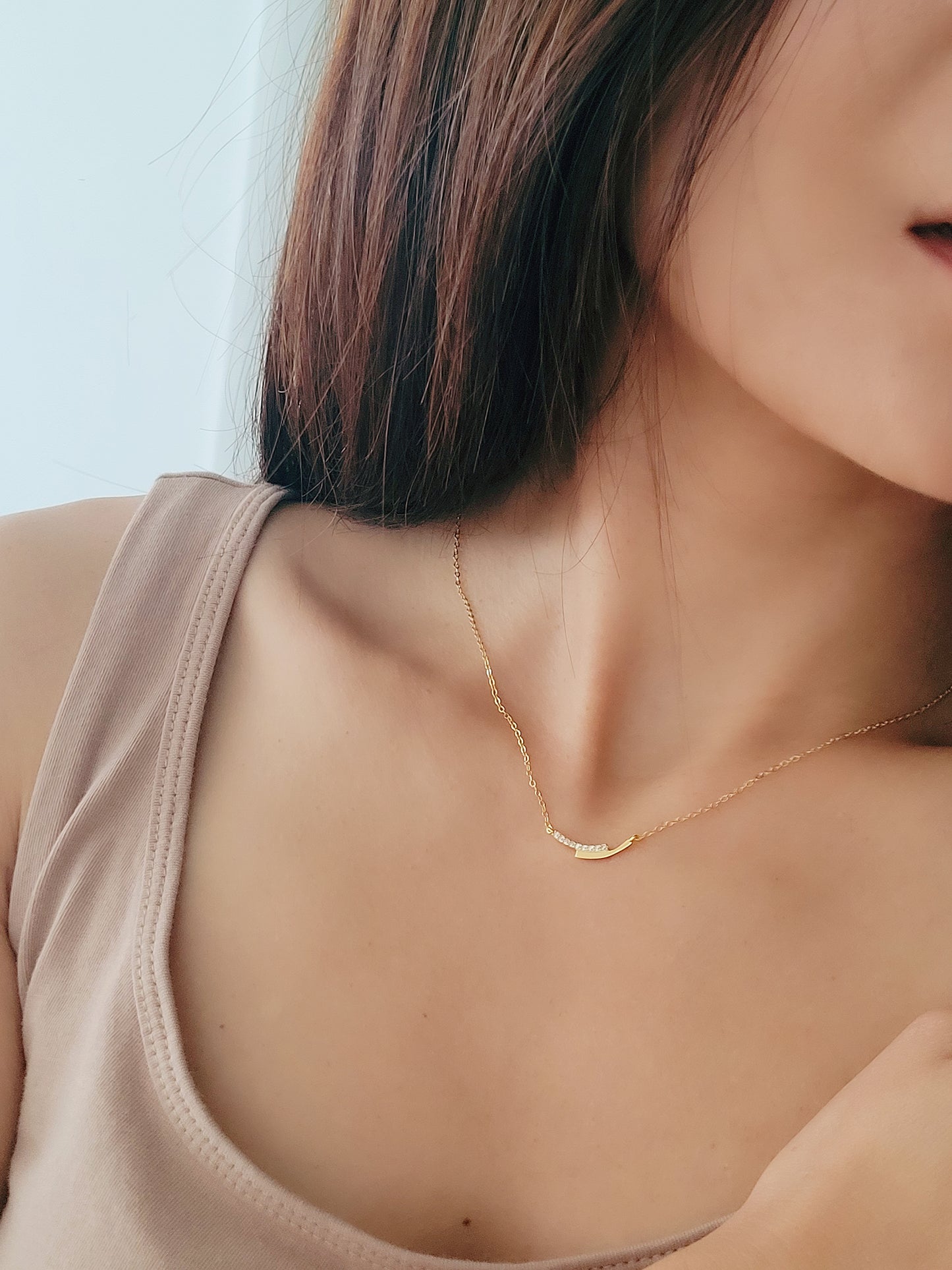 Woman wearing a delicate gold bar necklace in beige casual outfit, minimalist yet elegant.