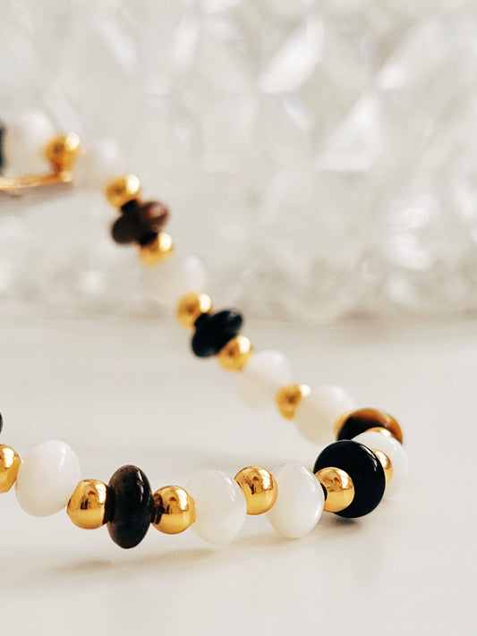 Close up of a gemstone bracelet featuring tiger's eye, mother of pearl, and black onyx beads with 22k gold vermeil accents