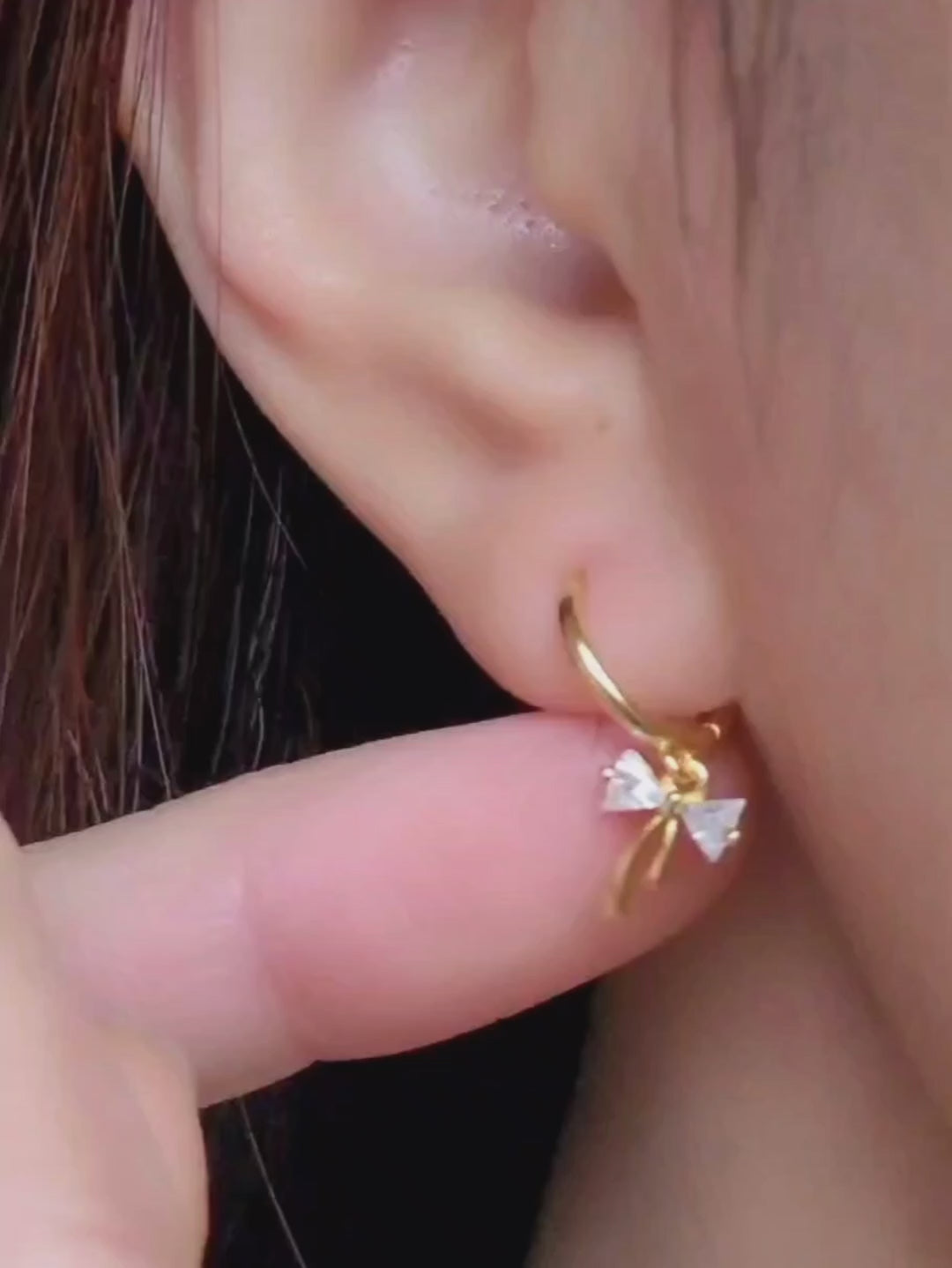 Close-up view of a woman's ear wearing gold ribbon bow earring with a dangling design, perfect for gifting to girlfriends, daughters, or loved ones.