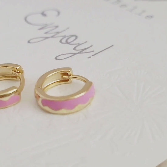 Details of a pair of chic pink enamel huggie hoops with a unique wavy pattern in 18K gold plating, perfect for adding a pop of color.