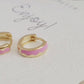 Details of a pair of chic pink enamel huggie hoops with a unique wavy pattern in 18K gold plating, perfect for adding a pop of color.