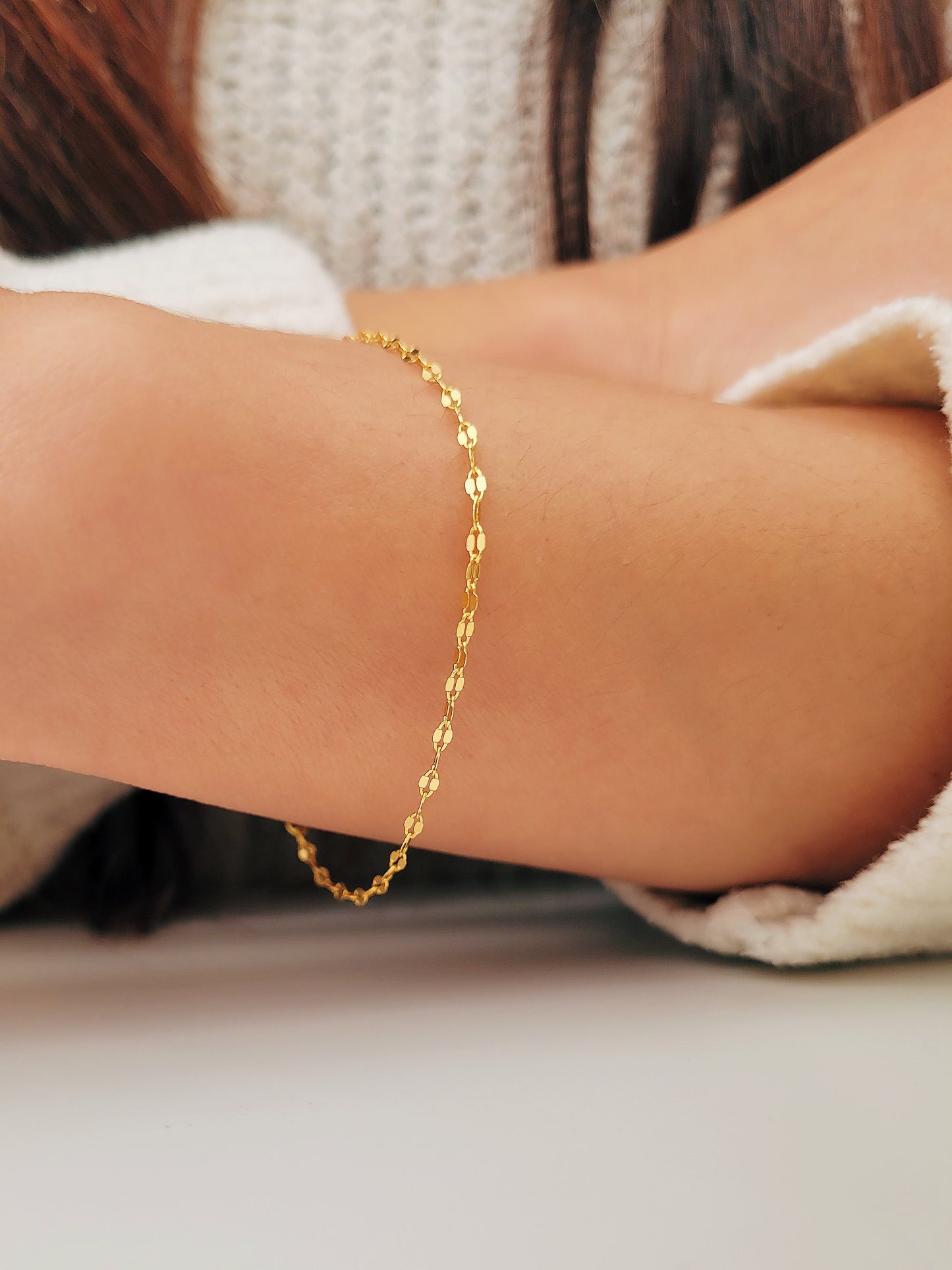 Woman wearing a delicate, gold vermeil skinny chain bracelet on her wrist, adding a subtle shimmer to her cozy. The bracelet's light-reflecting quality highlights its minimalist design, creating an elegant and understated style.
