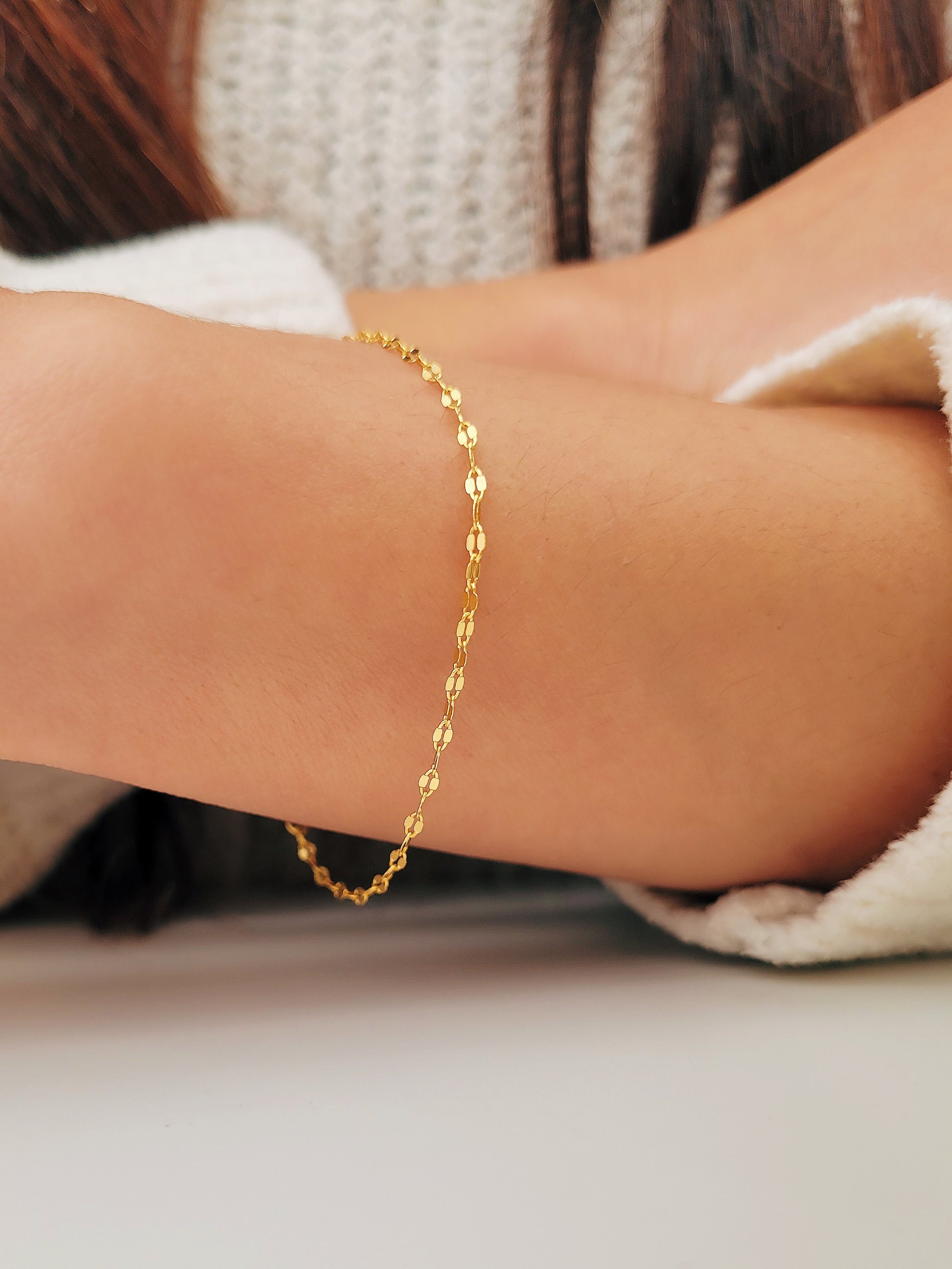 Woman wearing a delicate, gold vermeil skinny chain bracelet on her wrist, adding a subtle shimmer to her cozy. The bracelet's light-reflecting quality highlights its minimalist design, creating an elegant and understated style.