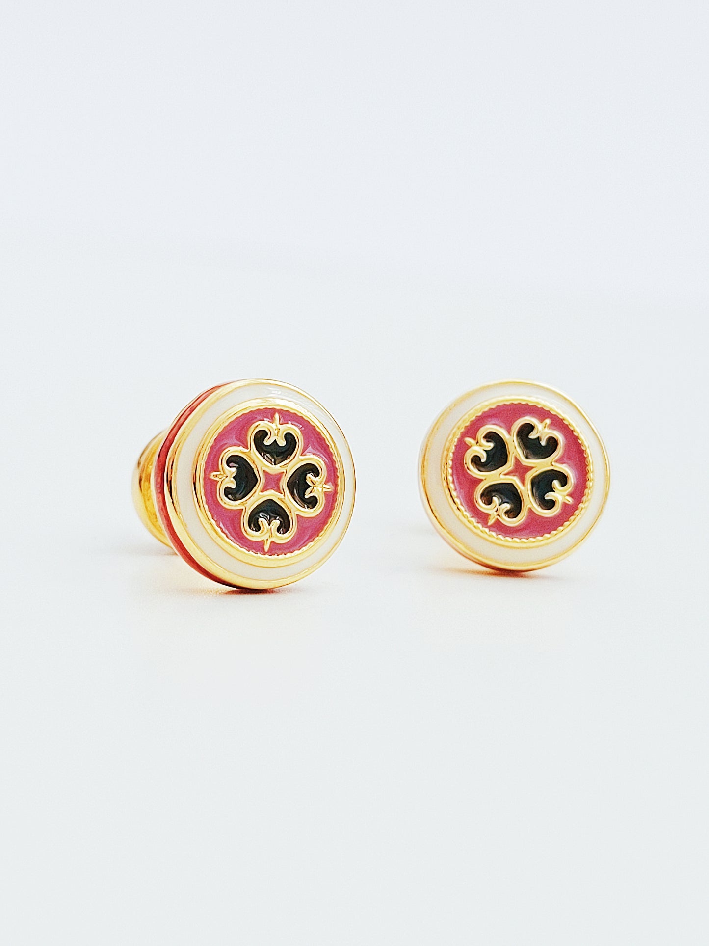 Closeup of retro-style stud earrings featuring a pink and dark green geometric tile pattern with gold accents. These vintage-inspired enamel earrings offer a classic, timeless design adding a touch of elegance to any outfit.