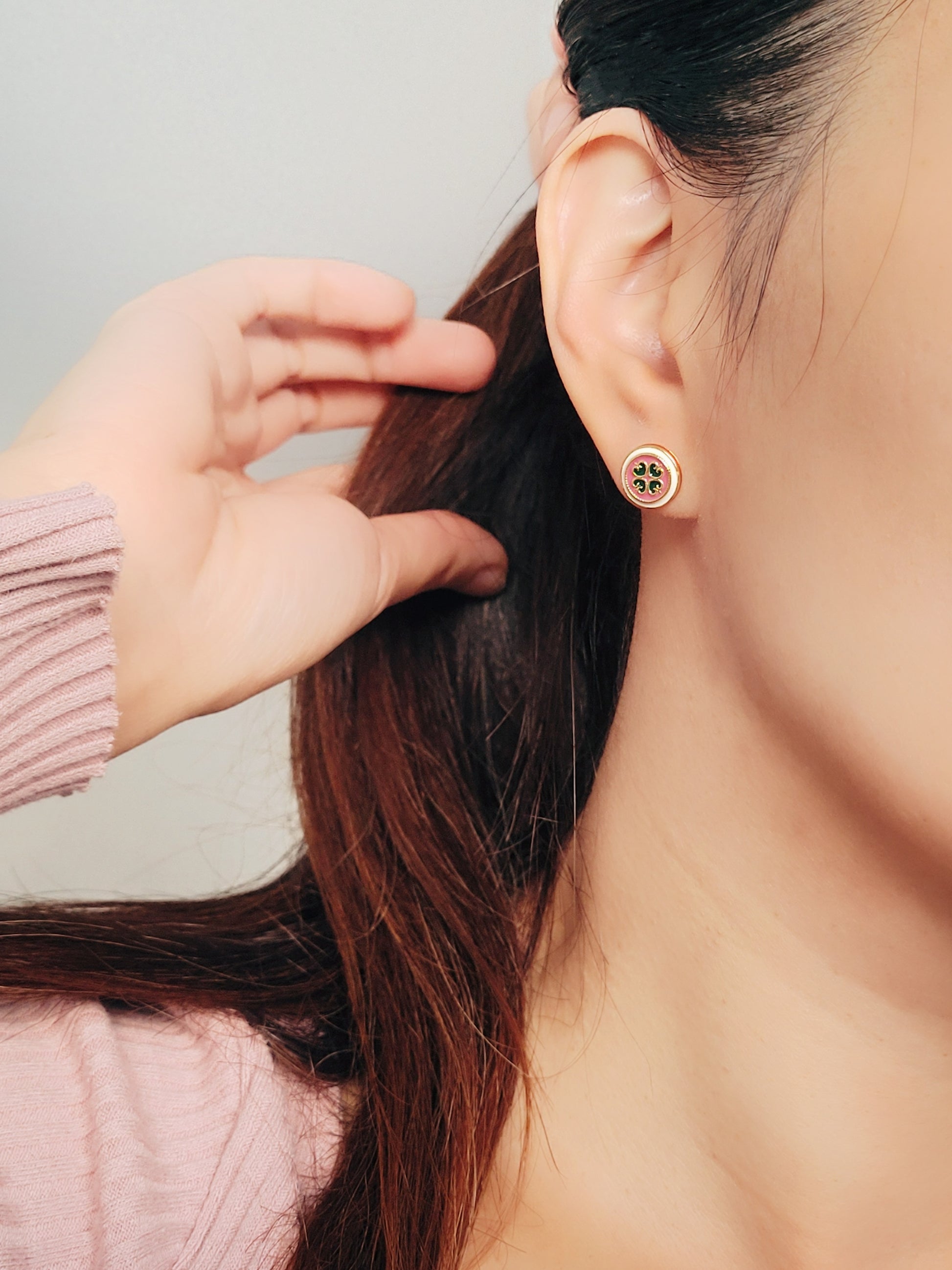 Close-up of a woman's ear wearing a pair of Retro Gothic tile pattern enamel stud earrings in pink, dark green, and gold. The intricate design features a vintage-style pattern with a bold color combination, creating a striking and elegant look.