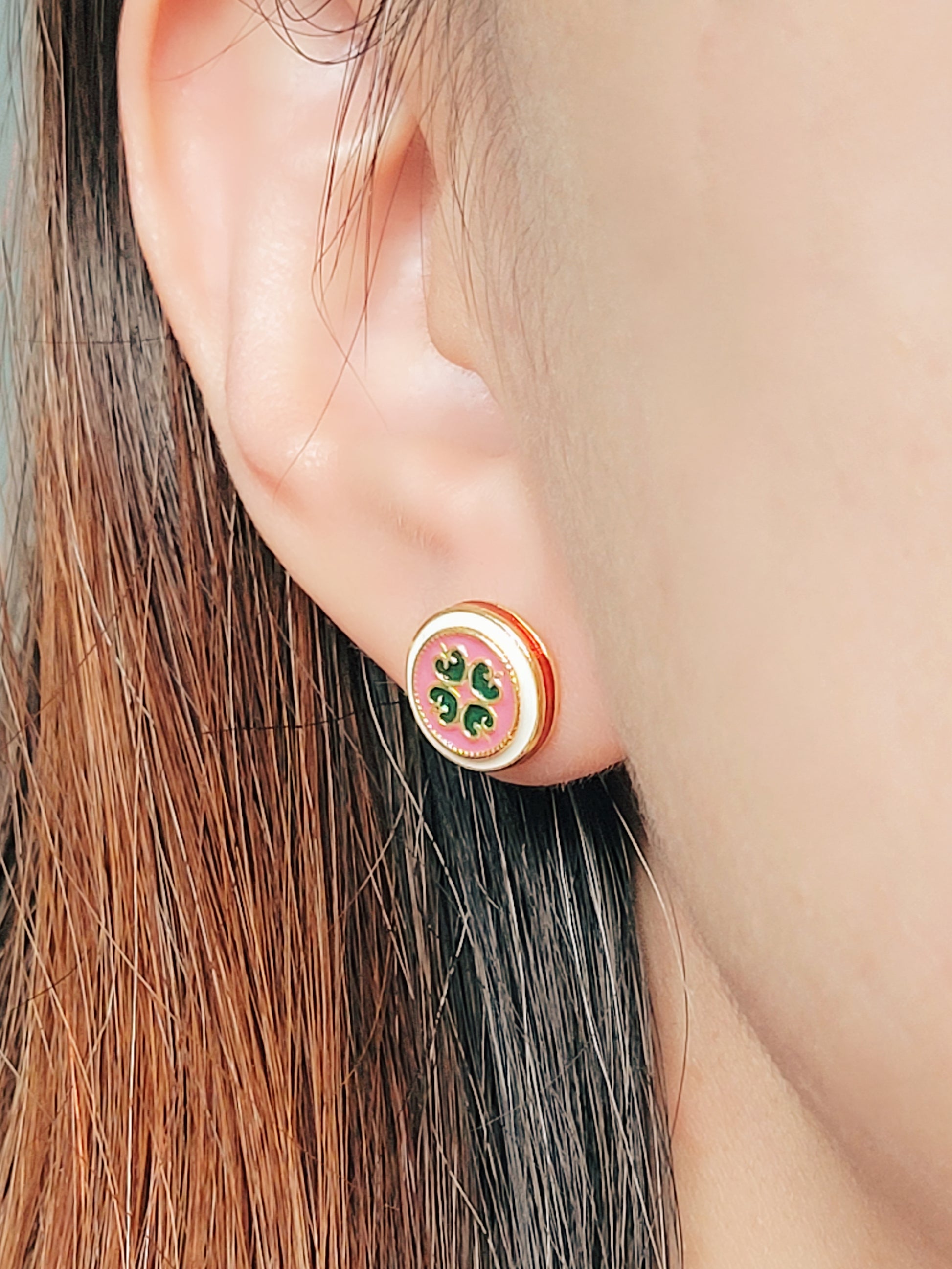Close-up of a woman’s ear wearing a pair of Retro Gothic tile pattern enamel stud earrings in pink, dark green, and gold. The intricate design features a vintage-style pattern with a bold color combination, creating a striking and elegant look.