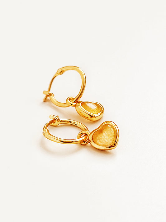 Gold heart dangle earrings with yellow crystal quartz gemstone on a light beige background